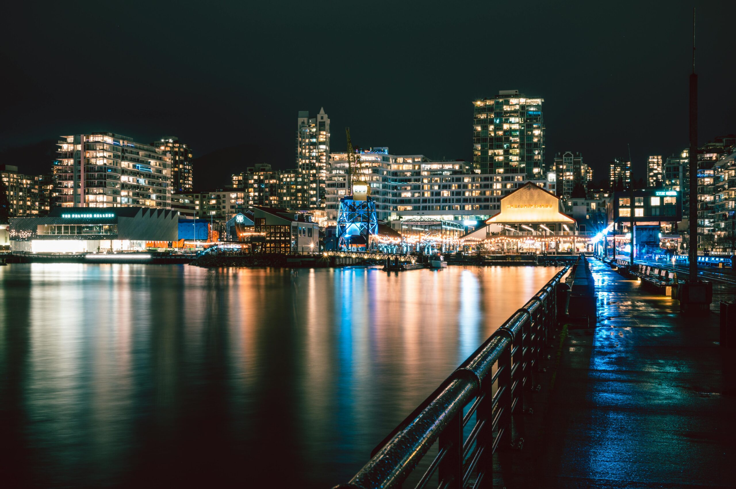 Illuminated waterfront skyline in North Vancouver captured by night, reflecting modern architecture and city lights.