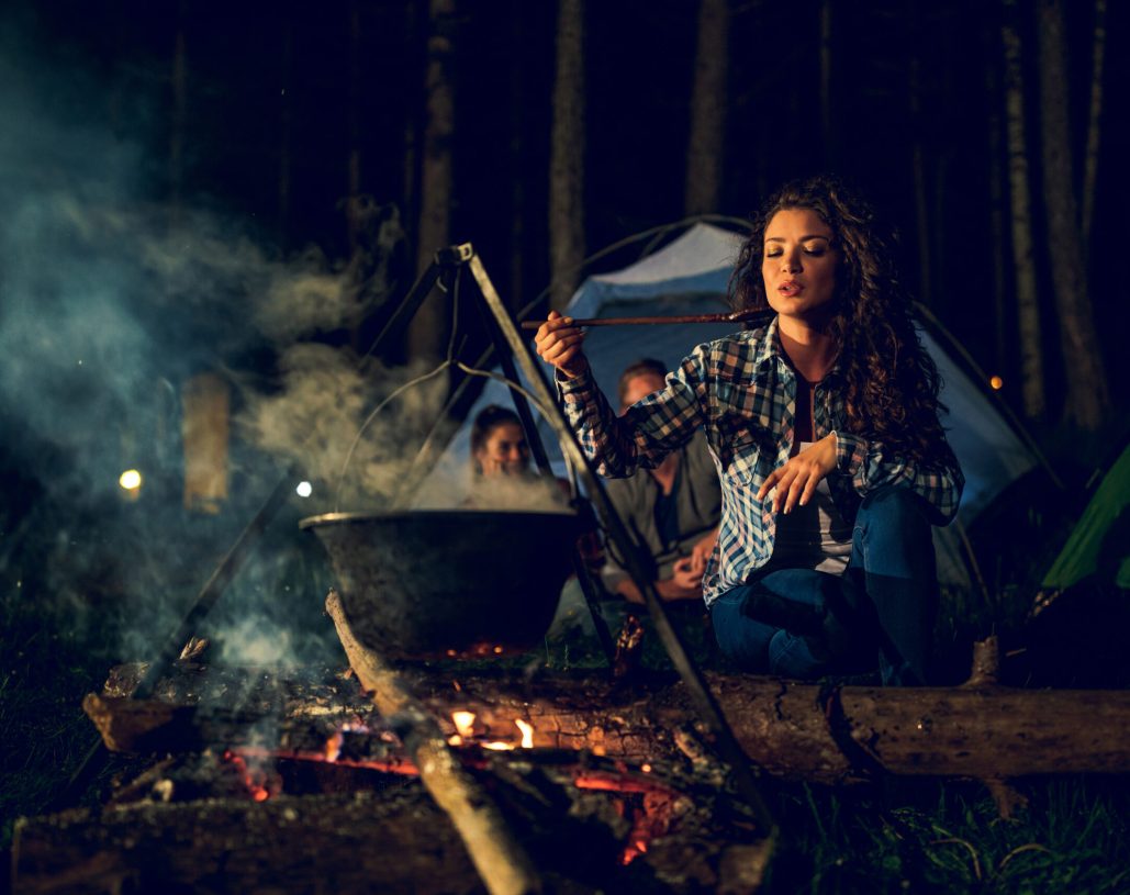Shot of an attractive young woman cooking dinner while camping with her friends in the woods.